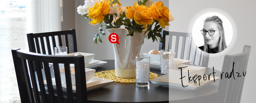 Jadalnia w stylu minimalistycznym z drewnianym, okrągłym stołem oraz czterema krzesłami. Na stole znajduje się biała zastawa oraz żółte kwiaty w wazonie.